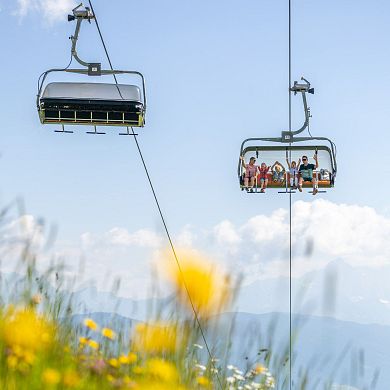 Familie fährt mit dem Sessellift durch blühende Almwiesen in Flachau während des Sommerurlaubs.