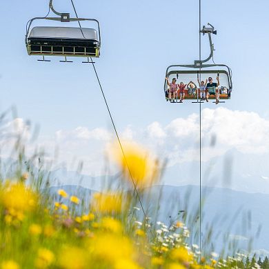 Familie fährt mit dem Sessellift durch blühende Almwiesen in Flachau während des Sommerurlaubs.