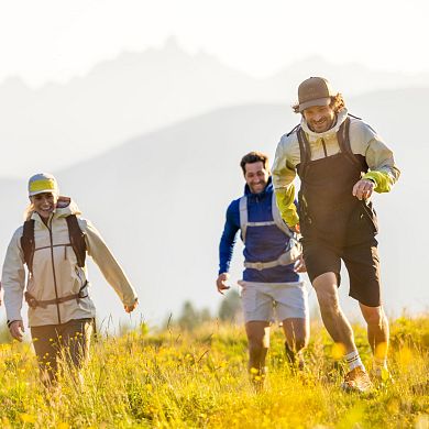 Vier Freunde beim Wandern im schönen Flachautal laufen über eine Wiese - im Hintergrund sieht man Bergsilhouetten.