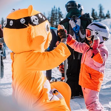 Kind gibt Maskottchen High-Five beim Skifahren am Shuttleberg in Flachauwinkl.